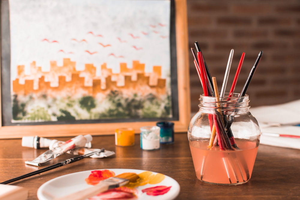 Sunlit creative studio featuring a blank canvas, paintbrushes in glass jars, and a mood board with sketches and color swatches.