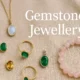 Close-up of assorted gemstone jewellery including rings, necklaces, and bracelets displayed on a soft fabric background.